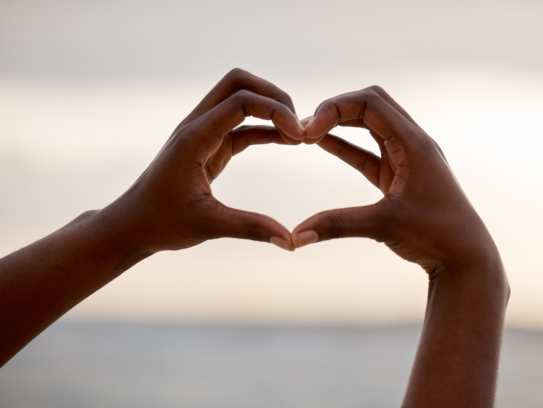 hands making a heart with sunset across the sea in the background