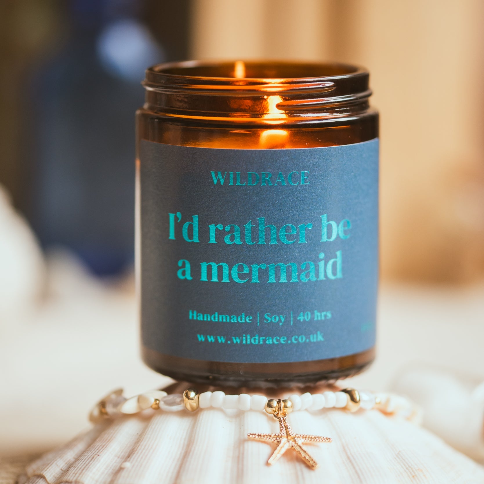 Candle in an amber jar with a blue label on a shell, surrounded by seashells.