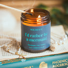 Candle with a label reading 'I'd rather be a mermaid' on top of a book.