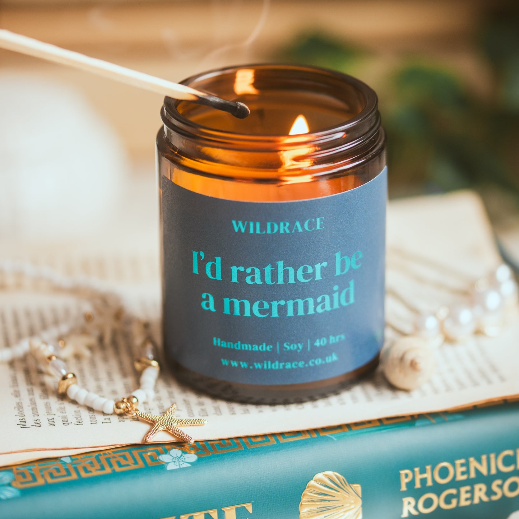 Candle with a label reading 'I'd rather be a mermaid' on top of a book.