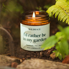 Candle in an amber jar with a label reading 'I'd rather be in my garden' surrounded by greenery.