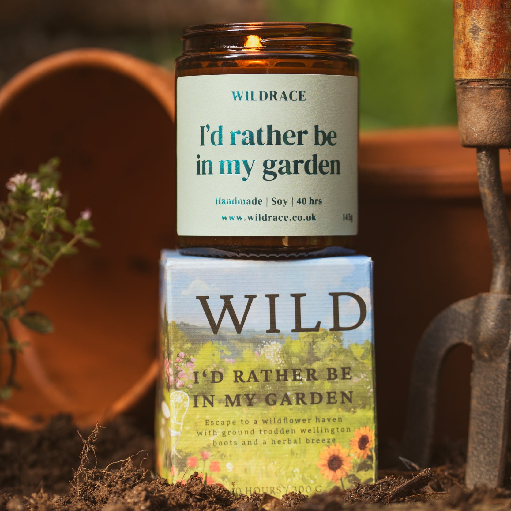 Candle and packaging labeled 'I'd rather be in my garden' by Wildrace on a garden-themed background.