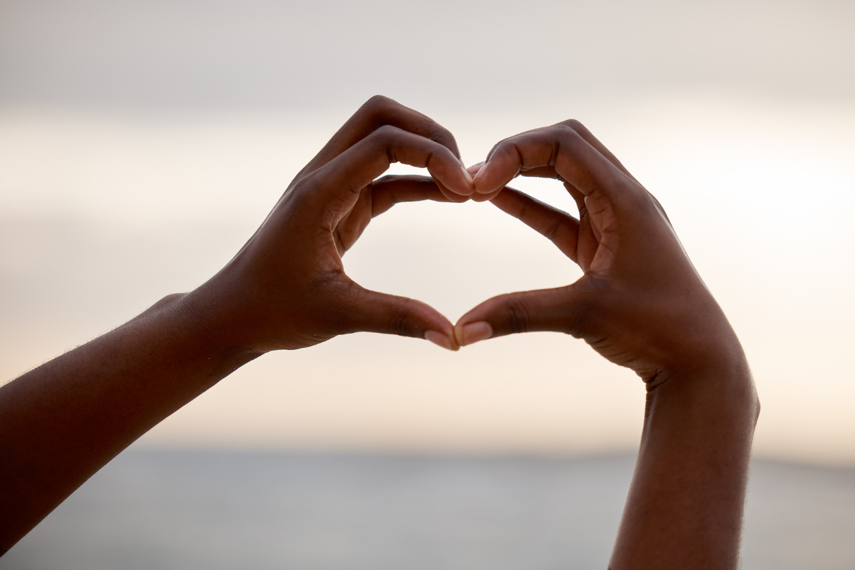hands making a heart with sunset across the sea in the background
