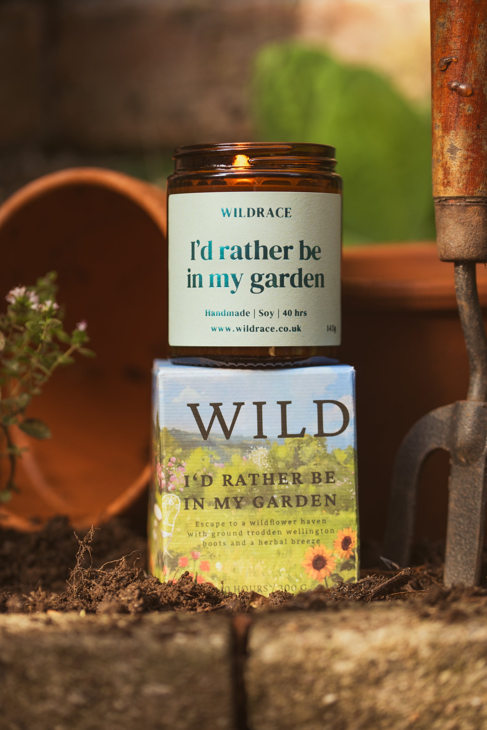 Candle and packaging labeled 'I'd rather be in my garden' by Wildrace on a garden-themed background.